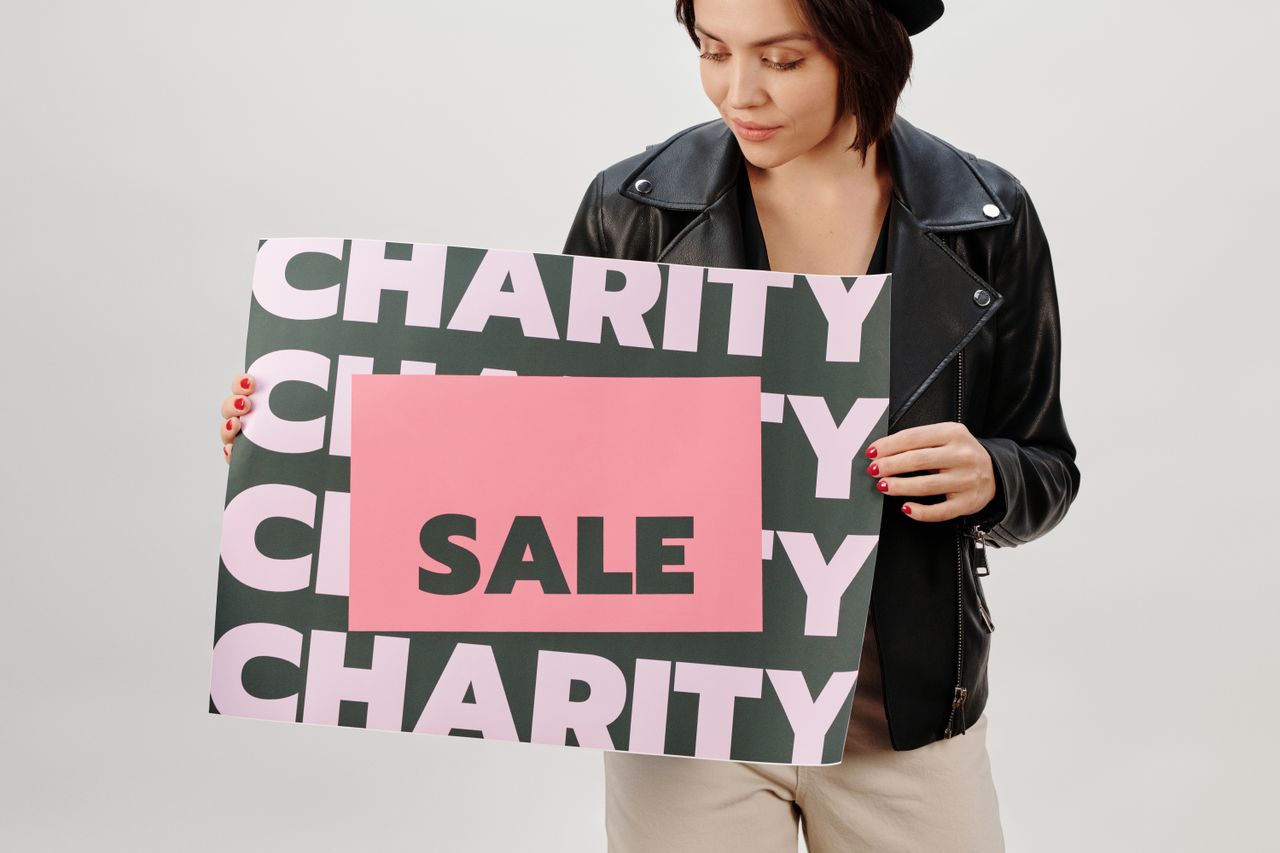 about-02 Woman holding a charity sale sign in a studio setting.