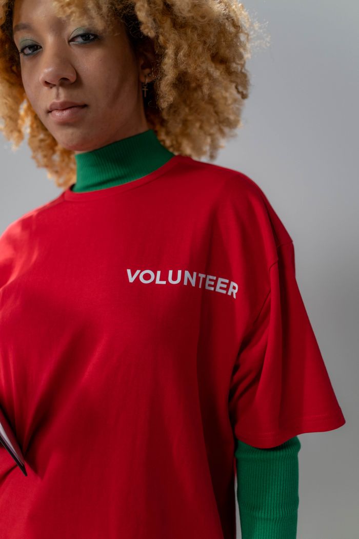 our-experience Confident young woman wearing a red volunteer t-shirt and green turtleneck, showcasing empowerment.
