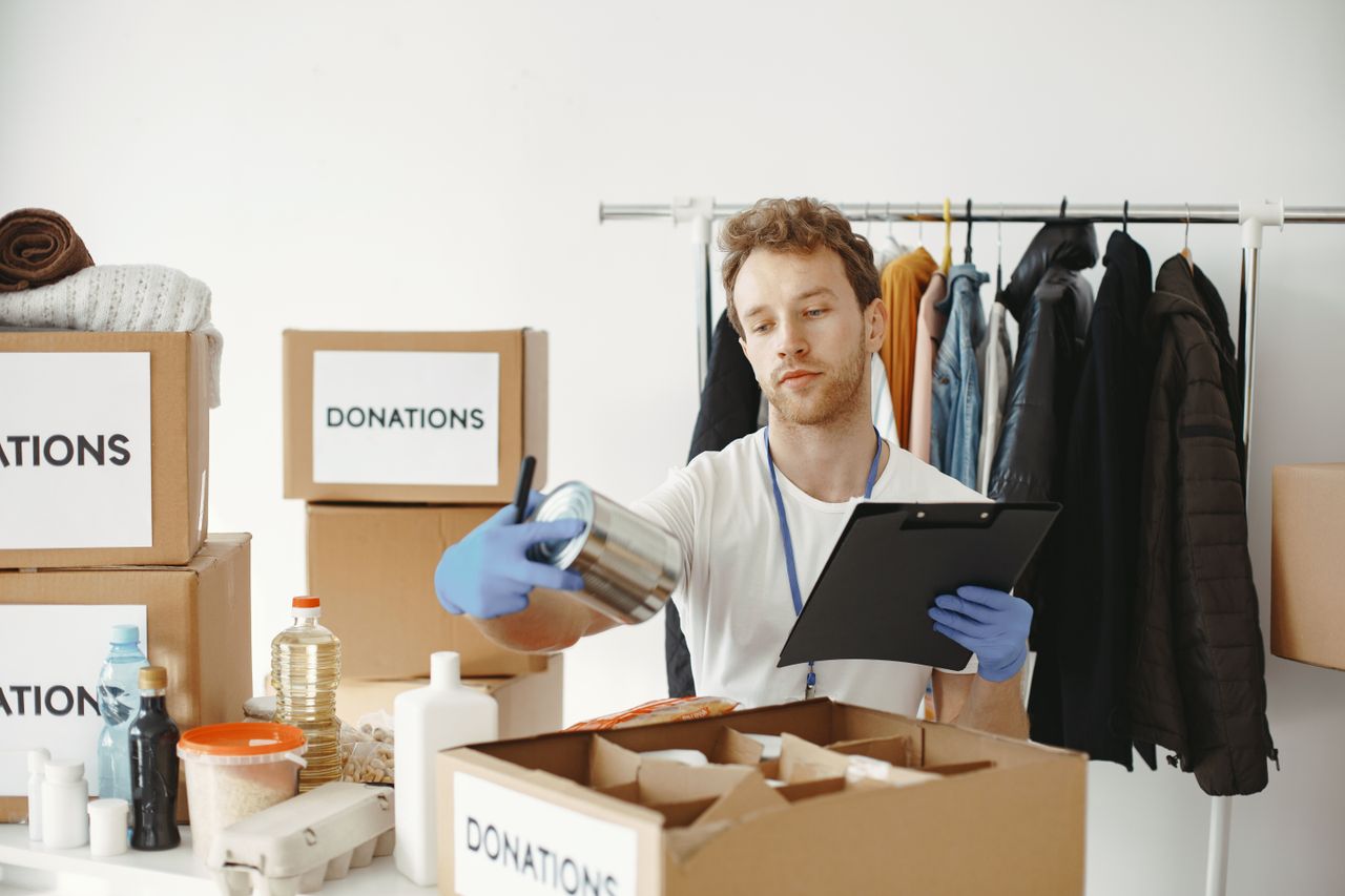 ours-journey A volunteer organizes food and clothing donations in a community center, maintaining records on a clipboard.